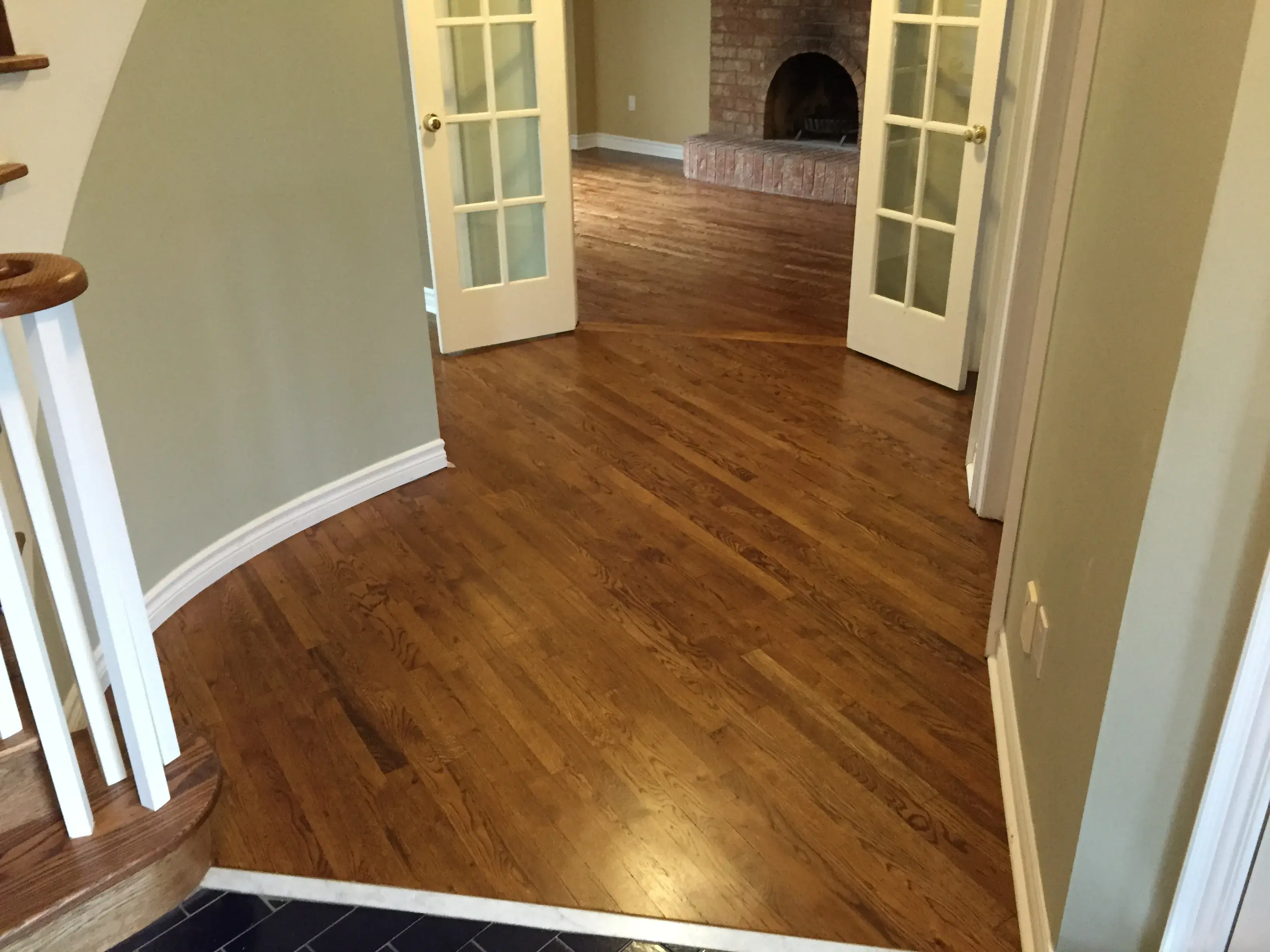 Refinished hardwood floor leading into a room with a brick fireplace